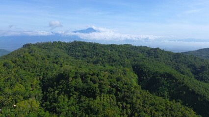 Dramatic Aerial drone view of hills with lush green trees with morning mist above with a background of rows of mountains