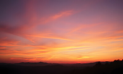 Fototapeta premium Orange sunset sky with distant mountain silhouettes. Perfect for nature-themed designs, travel brochures, outdoor adventure promotions, or inspirational content