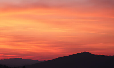 Obraz premium Orange sunset sky with distant mountain silhouettes. Perfect for nature-themed designs, travel brochures, outdoor adventure promotions, or inspirational content