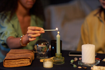 Unrecognizable gen Z girl lighting up candle during witchcore party with her friends, medium closeup