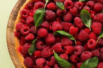 Berry pie with raspberries and basil leaves on wooden plate on light green background, close up