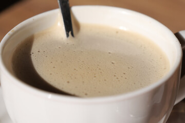 Warm cup of coffee with frothy milk on wooden table