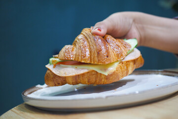 Hand holding a croissant sandwich with fresh ingredients © Towfiqu Barbhuiya 