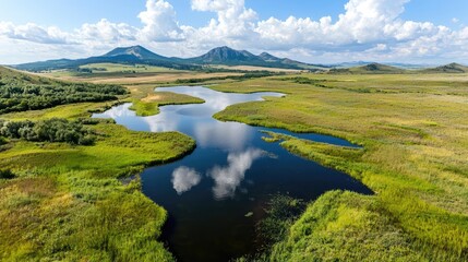 Obraz premium Aerial view of a tranquil lake reflecting clouds, surrounded by lush green vegetation and distant mountains; ideal for nature documentaries