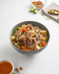 A bowl filled with rich soup featuring chunky meat, vibrant vegetables, and a tangy lime on the side, perfect for a warm meal