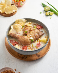 A hearty bowl of flavorful soto ayam or chicken soup garnished with crispy chips, herbs, and lime, perfect for a comforting meal