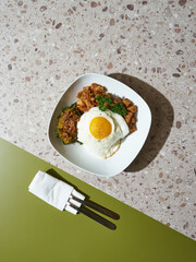 A plate holds a fried egg on chicken and broccoli, with neatly placed cutlery, showcasing a modern dining setup