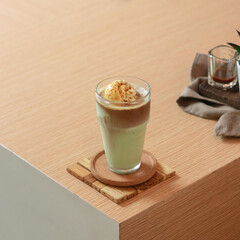 A delightful green tea beverage with creamy ice cream rests on a wooden table in a warm cafe, surrounded by a casual atmosphere