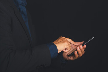 Businessman using smartphone in dark room, hands typing on screen.