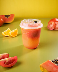 A tropical fruit drink centered in a vibrant setting is surrounded by fresh papaya slices and orange wedges, evoking a sunny, festive mood