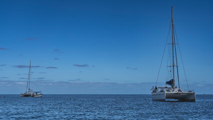 Boats in the blue ocean. White yachts, catamarans, a motorboat. Ripples on the surface. Silhouettes of people on board. Azure sky, clouds. Mauritius.