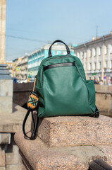 Stylish green leather backpack placed on stone ledge near city canal on sunny day. Urban background with classic architecture creates perfect blend of fashion and travel inspiration.