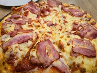 Thick crust pizza top with cubed ham, bacon and cheese on a wooden board