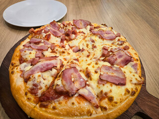 Thick crust pizza top with cubed ham, bacon and cheese on a wooden board