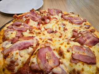 Thick crust pizza top with cubed ham, bacon and cheese on a wooden board