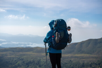 Fototapeta premium Trekker standing on a mountain ridge with a backpack and trekking poles, gazing at the scenic landscape