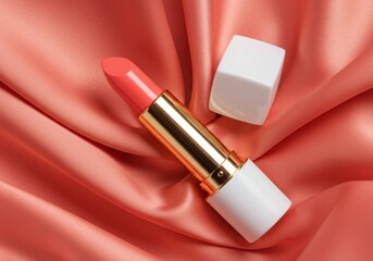 Obraz premium Luxury lipstick in coral pink shade with gold and white packaging on soft silky background in studio lighting