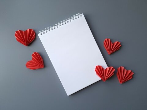 Blank notepad sheet and red paper ribbed hearts on grey background
