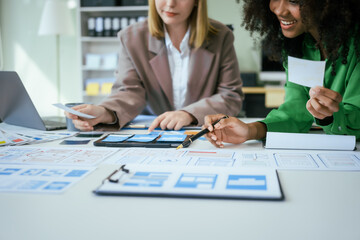 An African American businesswoman and a Caucasian woman collaborate at a desk, brainstorming...