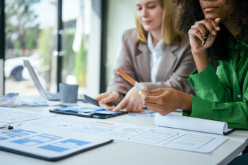 An African American businesswoman and a Caucasian woman collaborate at a desk, brainstorming...
