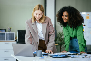 An African American businesswoman and a Caucasian woman collaborate at a desk, brainstorming...