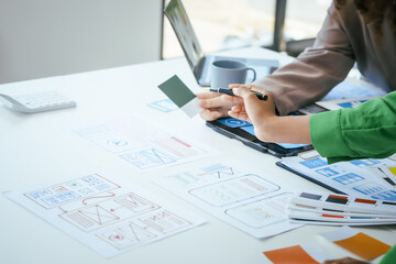 An African American businesswoman and a Caucasian woman collaborate at a desk, brainstorming...
