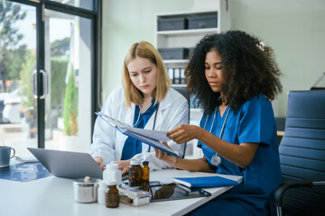 An African American female doctor and a white female doctor work at  hospital desk, discussing...