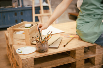 A happy Asian teenage girl painting with a brush on canvas at home, enjoying creativity and relaxation in a cozy, peaceful setting filled with artistic inspiration and vibrant colors