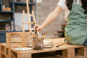 A happy Asian teenage girl painting with a brush on canvas at home, enjoying creativity and relaxation in a cozy, peaceful setting filled with artistic inspiration and vibrant colors