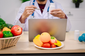 A male nutritionist sitting at a table, advising on healthy diets, promoting vegetable-based meals,...