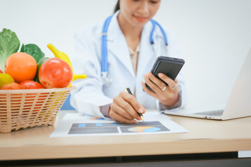 An Asian female doctor at her hospital desk works on a laptop, discussing the importance of eating...