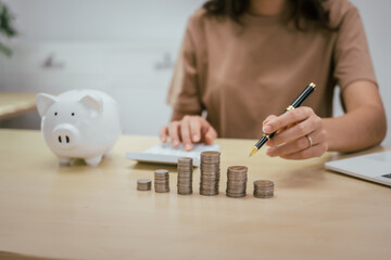A young woman saves money for the future by putting coins in a piggy bank on the table, managing...