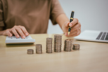 A young woman saves money for the future by putting coins in a piggy bank on the table, managing monthly expenses, and focusing on investment and business growth for financial stability