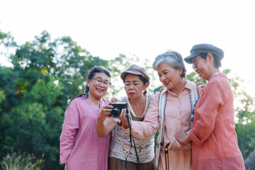 Senior Asian woman travels with close friend after retirement. Elderly checking camera screen reviewing captured photos laughing sharing joyful experience appreciating outdoor memories together.