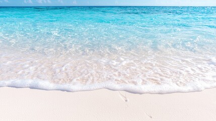 Obraz premium Gentle turquoise ocean wave washing onto a pristine white sand beach under bright daytime sunlight.