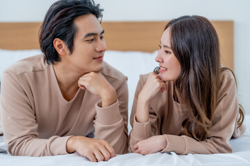 Young couple in casual outfits sharing moment on bed, smiling and gazing at each other with affection. Their connection is evident in their expressions