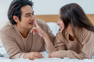 Couple enjoying playful moment on bed, sharing laughter and intimacy. Their cozy outfits and warm expressions create loving atmosphere