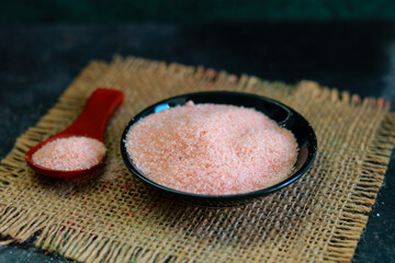 Pink Salt in a black bowl with wooden scoop on a dark background.