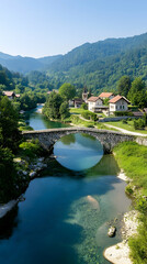 Fototapeta premium Stone bridge over calm river, village nestled in green valley, sunny day, idyllic travel postcard