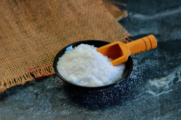 Salt in a black bowl with wooden scoop on a dark background.