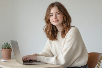 Naklejka premium A young woman with freckles smiles gently while working on her laptop at a desk.