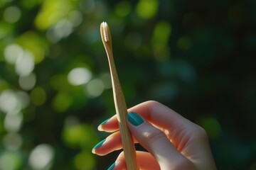 Woman's hand holding a bamboo toothbrush against a blurred green background.