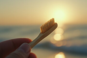 A hand holds a bamboo toothbrush at sunset by the ocean, promoting sustainable oral hygiene.