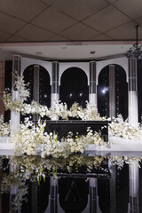 Banquet hall decor for a wedding. White flowers, mirrors and lighting. table setting and services of professional event organizers. 
