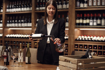 Female sommelier pouring red wine to decanter for decanting an alcoholic beverage, standing in...