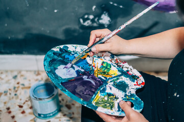 Creative Artist Blending Colors On A Palette With Brushes And Paint Cans Nearby - The Art Of...