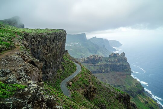 A breathtaking coastal landscape showcasing rugged cliffs, lush greenery, and a winding road overlooking the ocean under a cloudy sky.