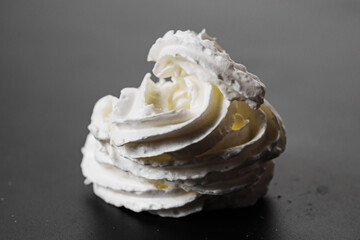 Whipped milk cream from the tube is squeezed onto a black surface. A delicious milk dessert.
