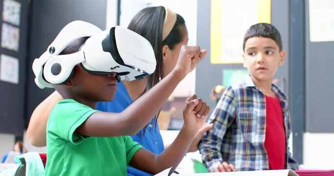 In school, boy using VR headset while teacher and classmate watching attentively