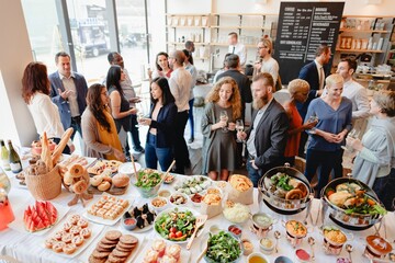 A diverse group of people at a buffet-style gathering, enjoying food and drinks. The event features...